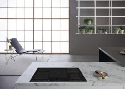 Piano cottura a induzione nero su isola in marmo bianco, ambiente elegante e luminoso.